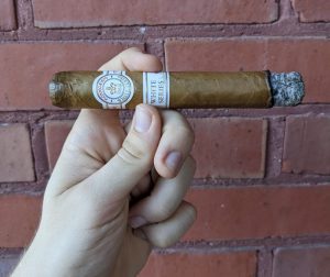 hand holding a Montecristo White Series toro cigar lightly-ashed