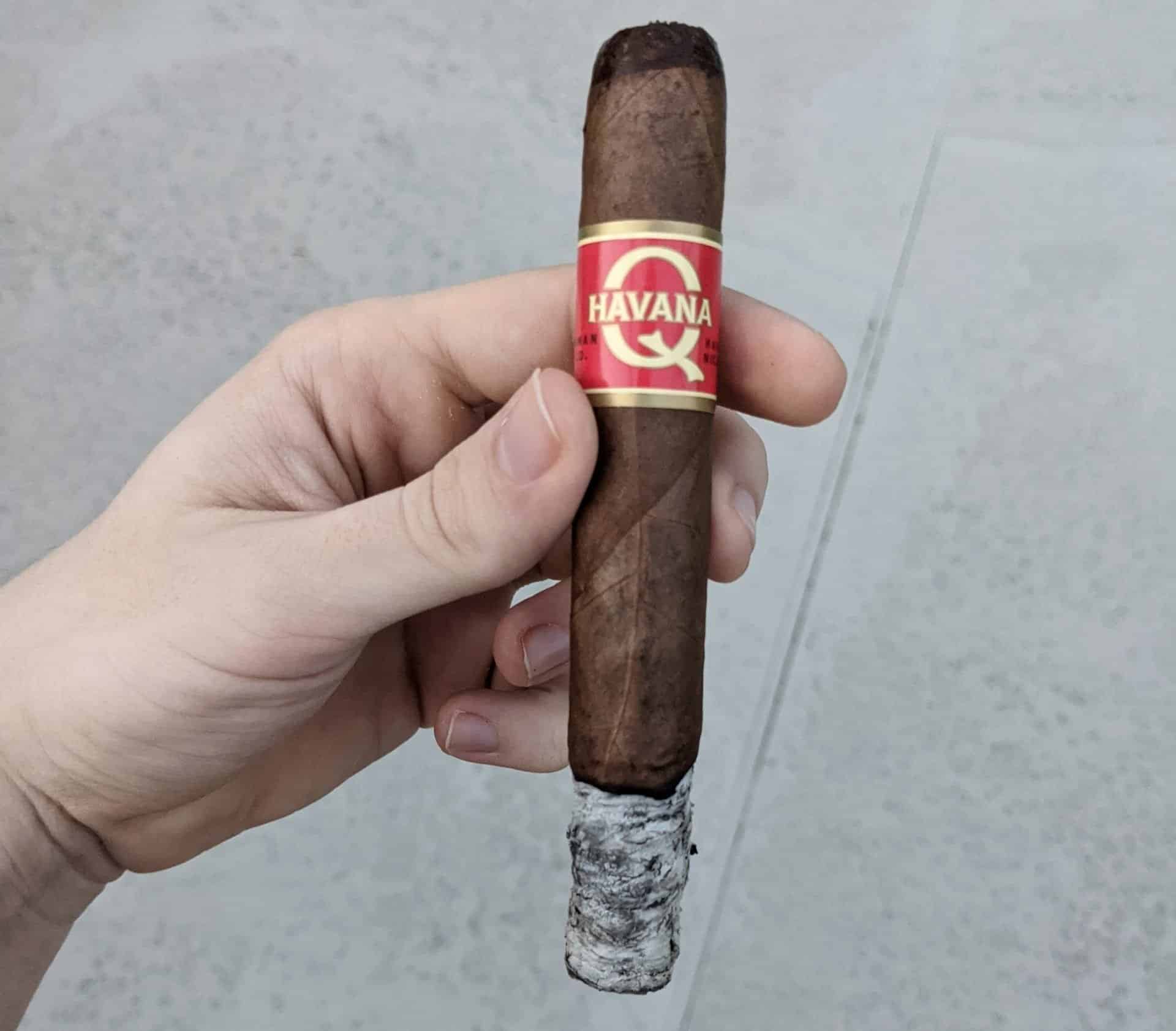 Hand holding a Havana Q Double Toro cigar ashed at the end